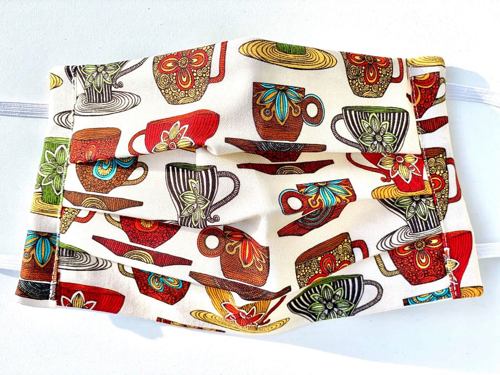 Teacups Mask Closeup | closeup cream fabric with multicoloured teacups and saucers design