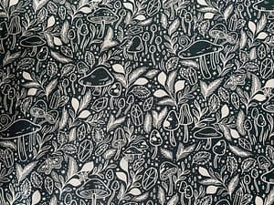Deep green fabric with pattern of mushrooms and various forest themes in white
