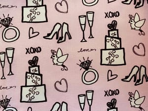 Pink fabric with pattern of wedding themed items like cake shoes glasses 